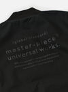 The master-piece x Universal Works Black Peached Poplin Newark Jacket is shown in a detailed close-up shot as a flat lay against a plain white background. The image focuses on the interior branding and construction, highlighting the master-piece x Universal Works dual-branded label and a white care instruction patch sewn onto the black fabric near a pocket.