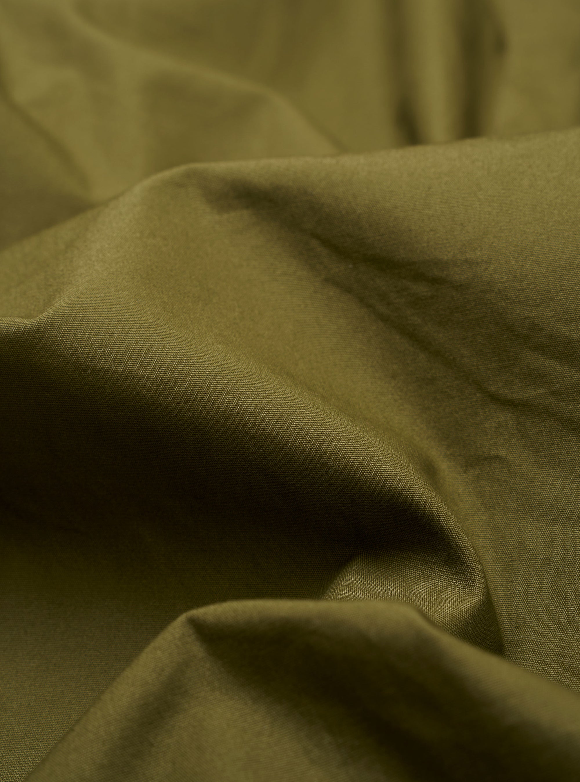 The master-piece x Universal Works Olive Recycled Poly Tech Tech Overshirt is shown in a detail view as a flat lay against a white background. The image highlights the back of the garment, focusing on the back yoke with a central box pleat and the technical texture of the olive green recycled fabric.
