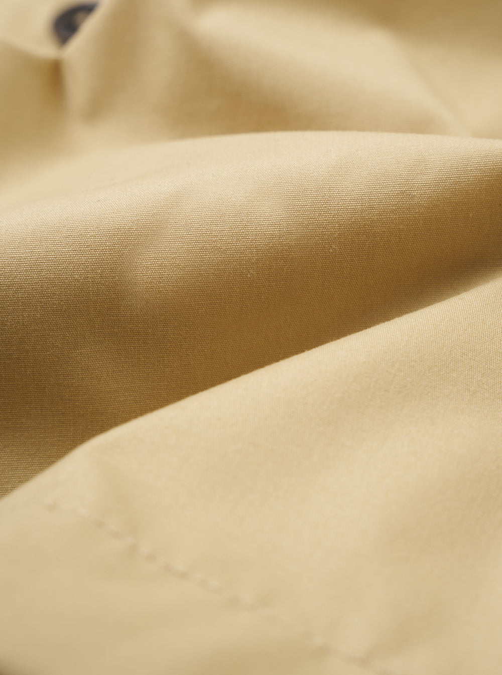 The master-piece x Universal Works Sand Recycled Poly Tech Tech Overshirt is shown from the back as a flat lay against a plain white background. The image highlights the garment's clean construction, featuring a back yoke with a central box pleat and a straight hem with an adjustable elasticated drawcord. The short-sleeved overshirt is made from a smooth, sand-colored recycled polytech fabric.