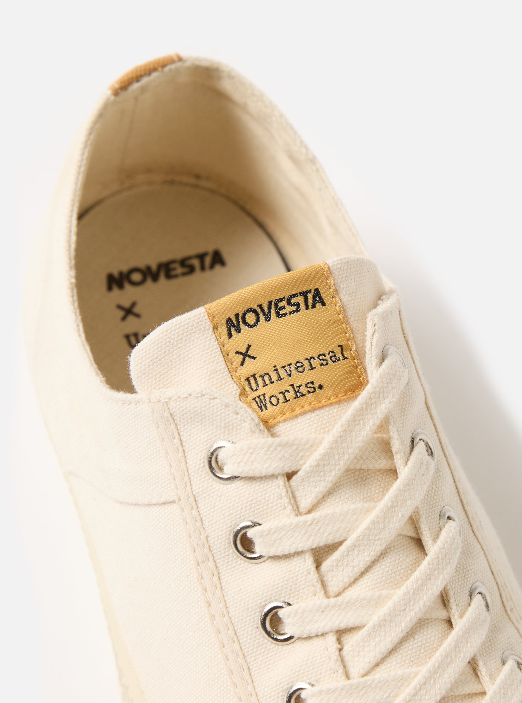 Close-up of the Novesta for Universal Works Ecru Canvas Star Master shoe. The ecru canvas and laces are visible, with a branded tongue. Shot on a white background.