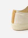 Close-up of the heel of a Novesta for Universal Works Ecru Canvas Star Master shoe. The canvas is off-white with a tan accent. The sole is textured. Shot on a white background.