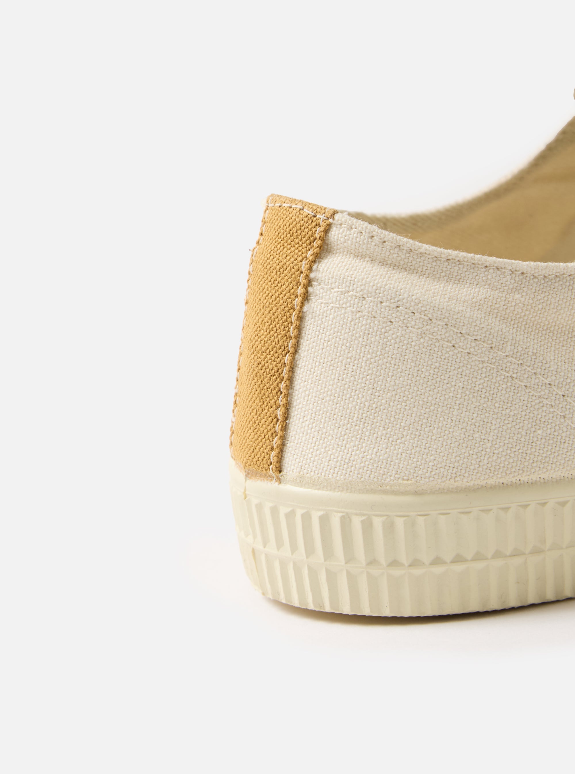 Close-up of the heel of a Novesta for Universal Works Ecru Canvas Star Master shoe. The canvas is off-white with a tan accent. The sole is textured. Shot on a white background.