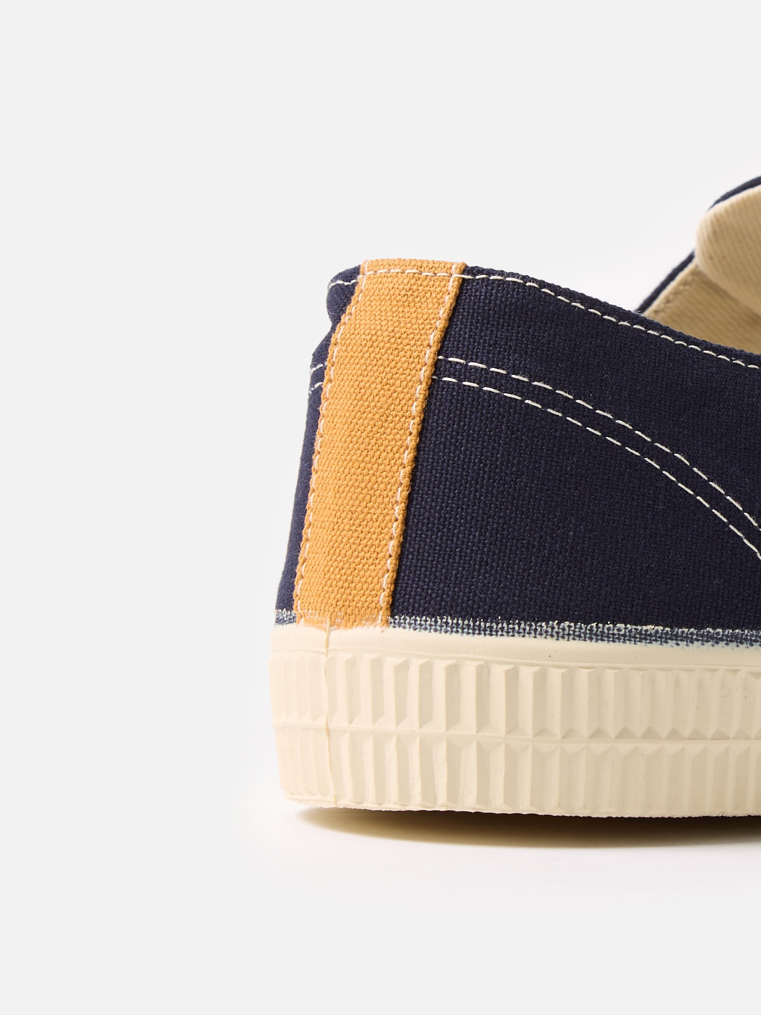 Close-up of the Novesta for Universal Works Navy Canvas Star Master shoe. Features navy canvas, mustard heel detail, and a textured white sole. Shot on a white background.