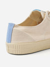 The Novesta for Universal Works Ecru/Pale Blue Canvas Star Master is shown from a side profile view against a white background. The low-top sneaker features an ecru cotton canvas upper with tonal stitching and silver-tone metallic eyelets. A distinctive pale blue heel strip provides a point of contrast, and the thick, textured natural rubber sole is ecru in color.