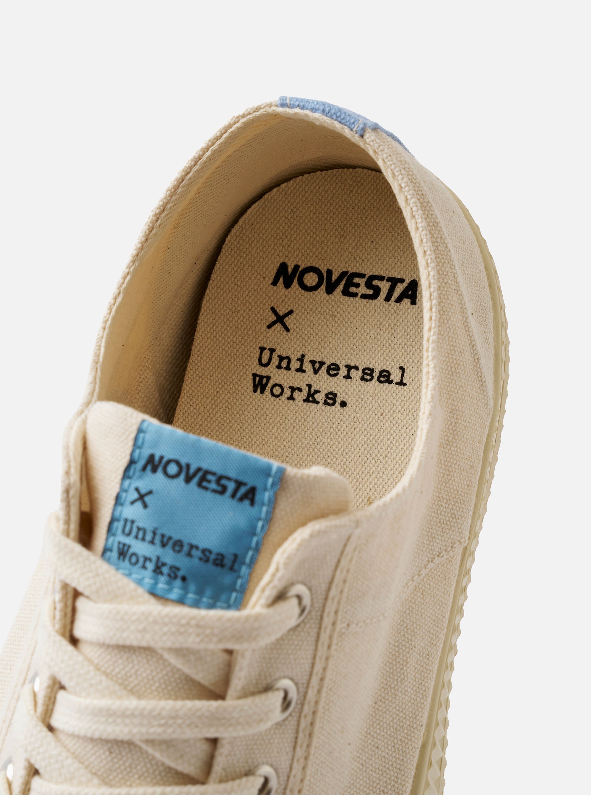 The Novesta for Universal Works Ecru/Pale Blue Canvas Star Master is shown from a side profile view against a white background. The sneaker features an ecru canvas upper with a contrasting pale blue heel strip and matching pale blue vulcanized rubber sole and toe cap. Chrome eyelets and ecru laces are prominent on the side-facing upper.