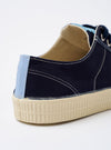 The Novesta for Universal Works Navy/Pale Blue Canvas Star Master is shown as a side view against a white background. The sneaker features a navy cotton canvas upper with contrast stitching, silver metallic eyelets, and navy laces. A prominent pale blue pull tab is located on the heel, and a dual-branded woven tag is visible on the tongue. The shoe has a chunky, textured ecru natural rubber sole and toe cap.