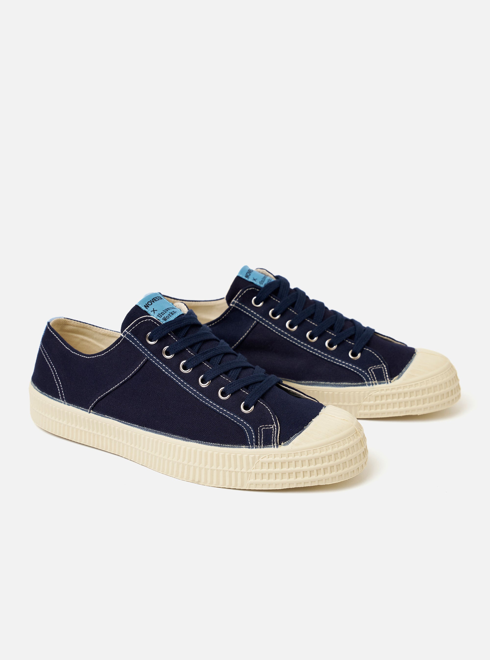 The Novesta for Universal Works Navy/Pale Blue Canvas Star Master is shown from a side profile against a white background. The sneaker features a navy cotton canvas upper with contrast ecru stitching and metallic eyelets. A prominent pale blue flash is visible on the heel, and the shoe is finished with a thick, textured ecru rubber vulcanized sole and toe cap.