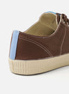 The Novesta for Universal Works Brown/Pale Blue Canvas Star Master shoe is shown from a side profile view against a plain white background. The sneaker features a brown cotton canvas upper with contrast stitching, metallic eyelets, and a chunky, textured ecru vulcanized rubber sole. A distinctive pale blue pull tab is located on the heel, and a dual-branded woven tag is visible on the tongue.