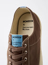 The Novesta for Universal Works Brown/Pale Blue Canvas Star Master shoe is shown from a side profile against a plain white background. The sneaker features a brown cotton canvas upper with contrast stitching, silver metallic eyelets, and tonal brown laces. It has a chunky ecru-colored vulcanized rubber sole with a matching rubber toe cap and a signature pale blue pull tab at the heel.