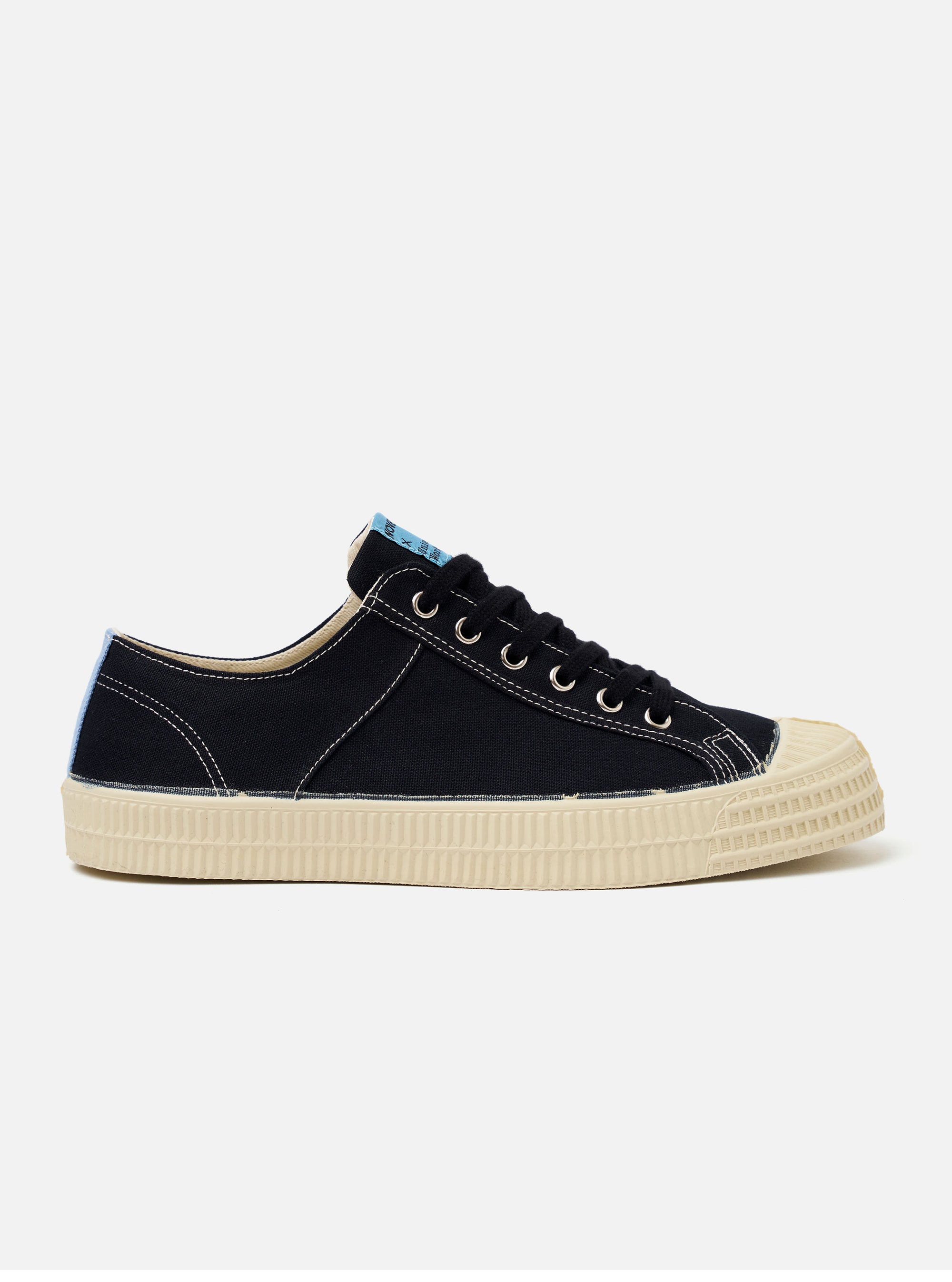 The Novesta for Universal Works Black/Pale Blue Canvas Star Master is shown from a side profile as a flat lay against a white background. The low-top sneaker features a black cotton canvas upper with contrast white stitching and metallic eyelets. A signature chunky ecru vulcanized rubber sole and toe cap are prominent, with a pale blue flash detail on the heel.
