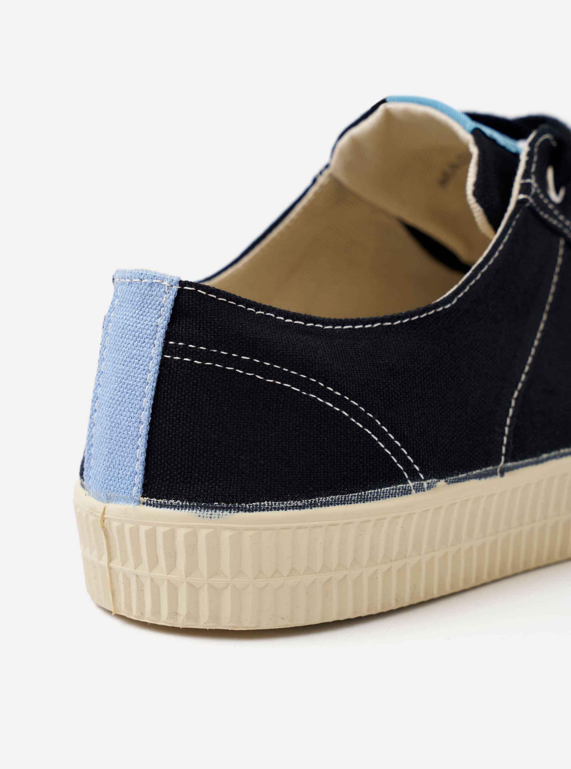 The Novesta for Universal Works Black/Pale Blue Canvas Star Master shoe is shown from a side profile against a white background. The sneaker features a black cotton canvas upper with contrast stitching, metallic eyelets with black laces, and a chunky ecru vulcanized rubber sole and toe cap. A distinctive pale blue pull tab is attached to the heel, and a dual-branded woven tag is visible on the tongue.