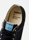 The Novesta for Universal Works Black/Pale Blue Canvas Star Master is shown in a side profile view against a white background. The sneaker features a black cotton canvas upper with matching black laces and metallic eyelets. It has a chunky, textured ecru rubber sole with a reinforced toe cap. A distinct pale blue vertical strip is visible on the heel.