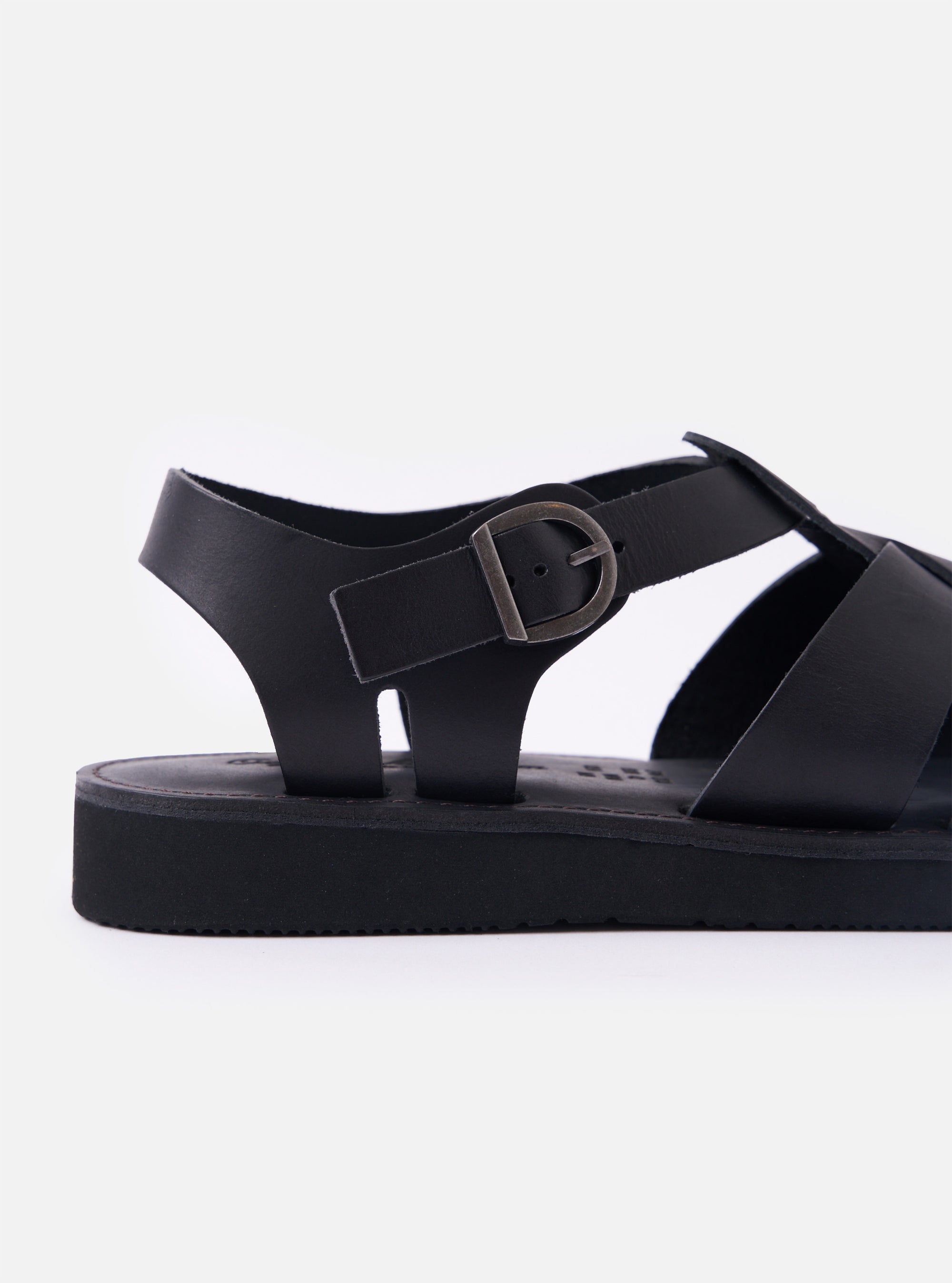 The Organic Handloom Black Leather Gurkha is shown from a side-angle view as a flat lay against a plain white background. The image highlights the shoe's profile, showcasing the woven leather strap design, the silver-tone metal buckle closure, and the thick, textured black foam rubber sole.