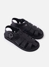 The Organic Handloom Black Leather Gurkha is shown from a high-angle view as a flat lay against a plain white background. The image focuses on the top and side of the footwear, highlighting the braided black leather strap construction, the silver-tone metal buckle closure, and the thick, textured foam rubber outsole.