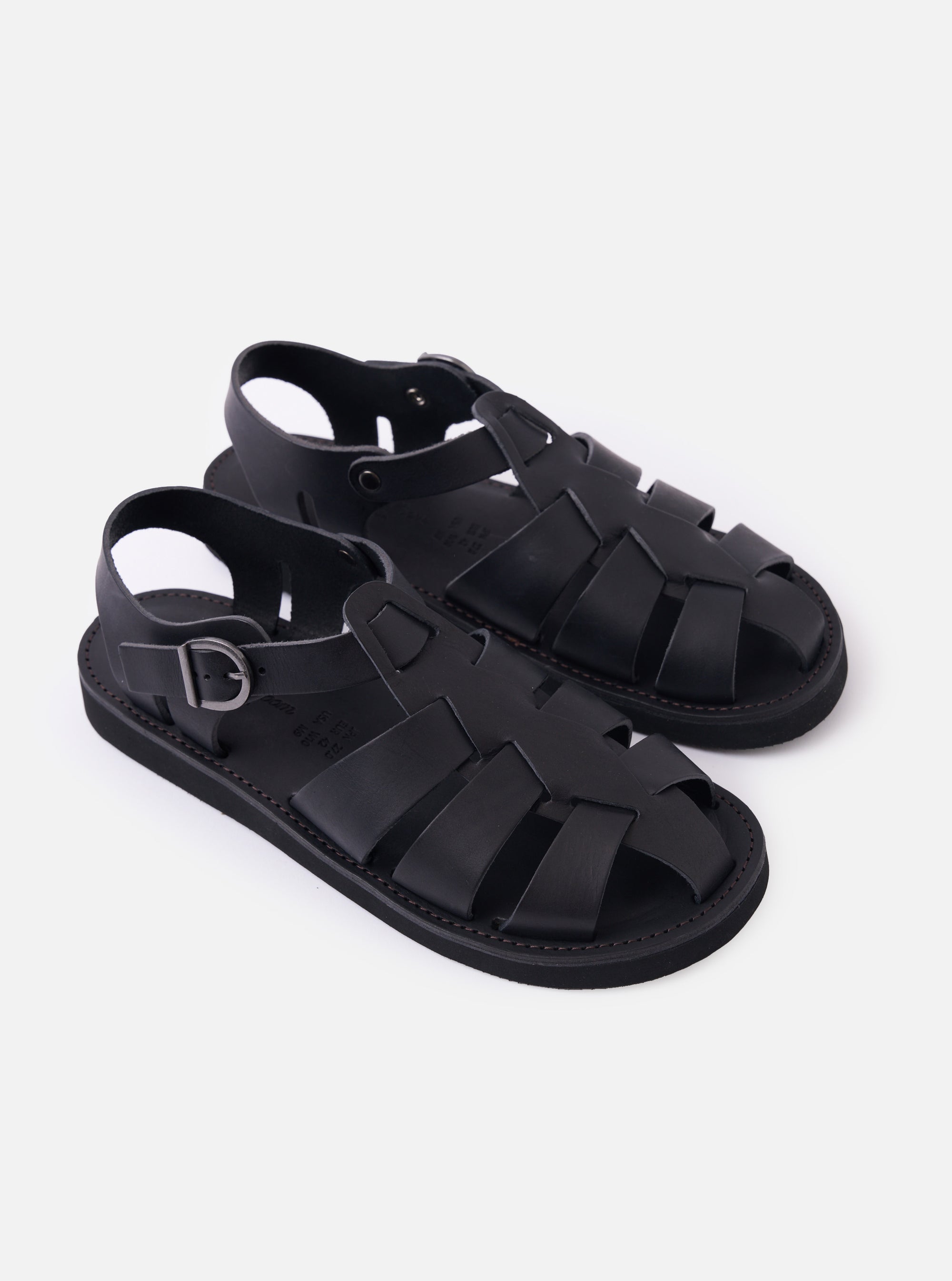 The Organic Handloom Black Leather Gurkha is shown from a high-angle view as a flat lay against a plain white background. The image focuses on the top and side of the footwear, highlighting the braided black leather strap construction, the silver-tone metal buckle closure, and the thick, textured foam rubber outsole.