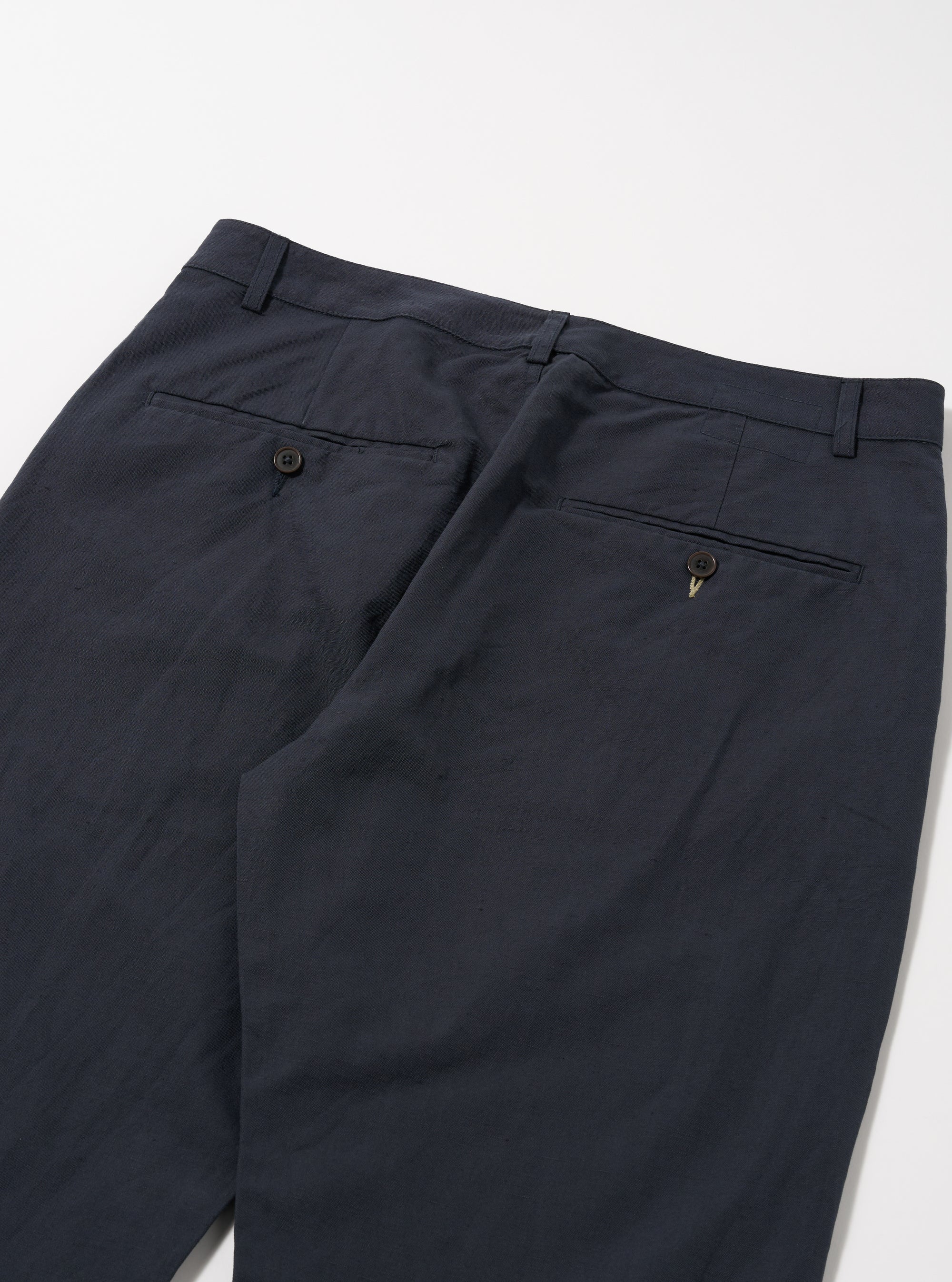 Close-up of the back of Navy Linen Slub Weave Military Chino pants on a white surface. The linen texture and button details are visible.