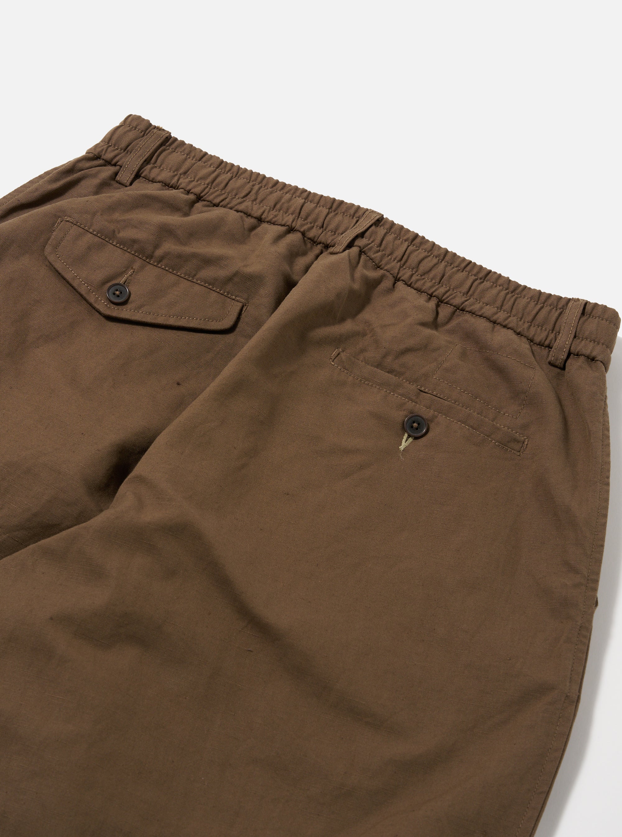 Close-up of the back of Khaki Linen Slub Weave Oxford Pant on a white surface. Shows the elastic waistband, back pockets with button closures, and the slub weave texture of the linen.