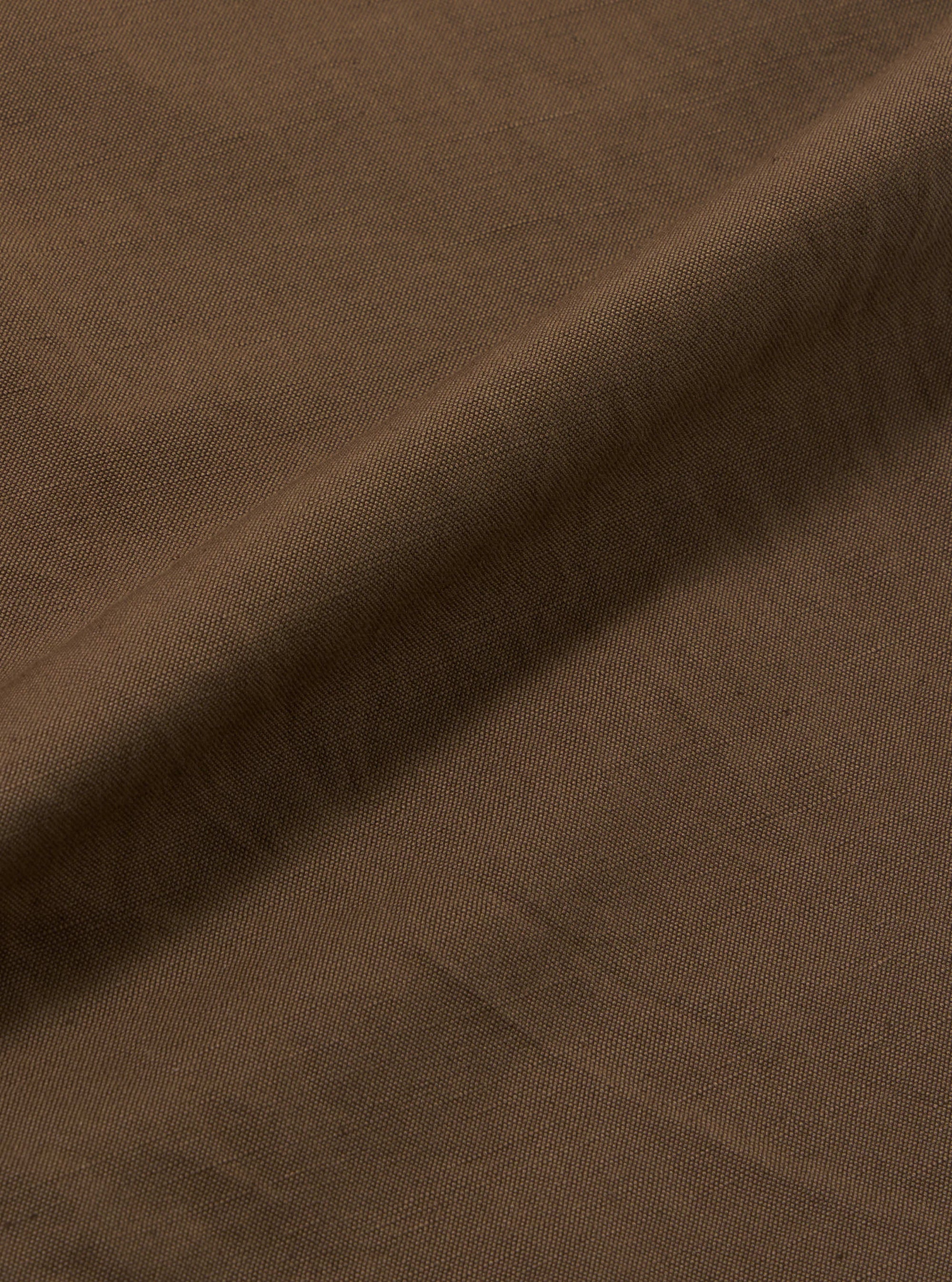 Close-up of the Khaki Linen Slub Weave Oxford Pant fabric. The material is a textured khaki linen, draped on a plain surface to show the weave.