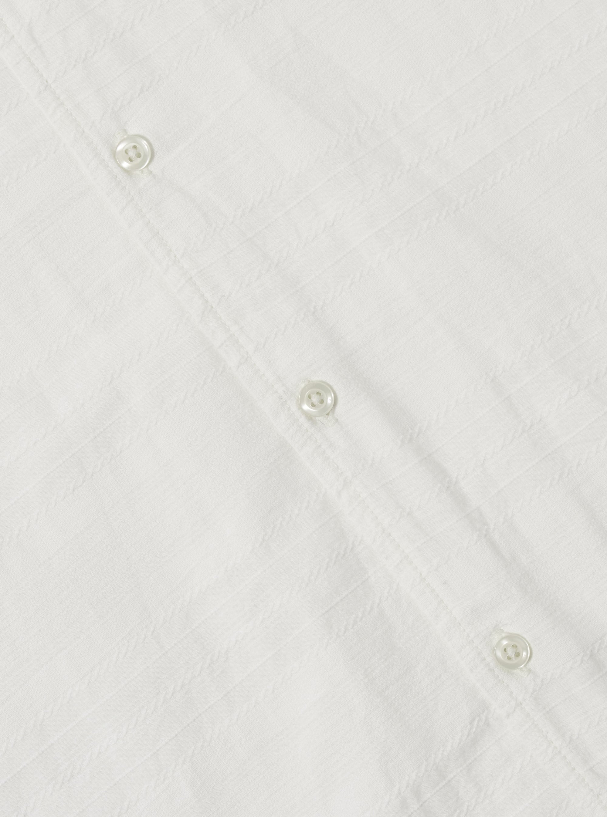 Close-up of the Ecru Deffe Self Stripe Minari Shirt, showing the ecru color, self-stripe texture, and button details. Shot on a flat surface.