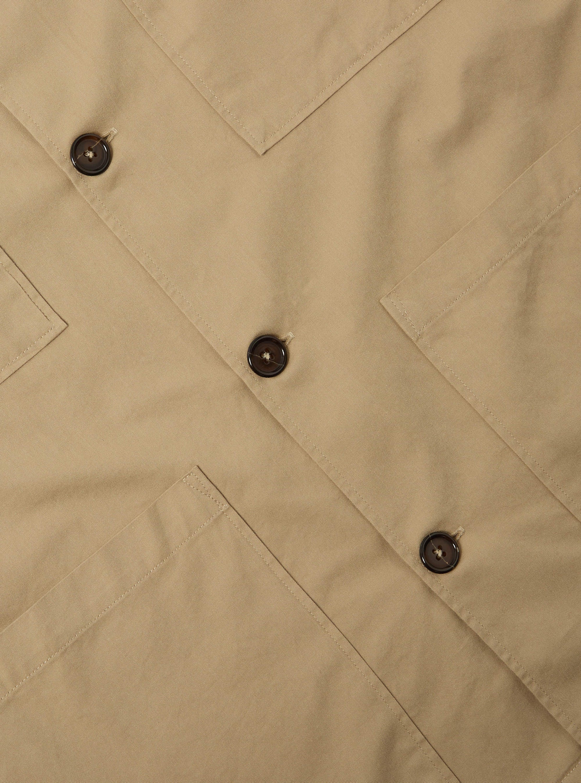 Close-up of the Sand Military Cotton Dockside Overshirt. The sand-colored cotton fabric features brown buttons and detailed stitching. Shot on a flat, neutral surface.