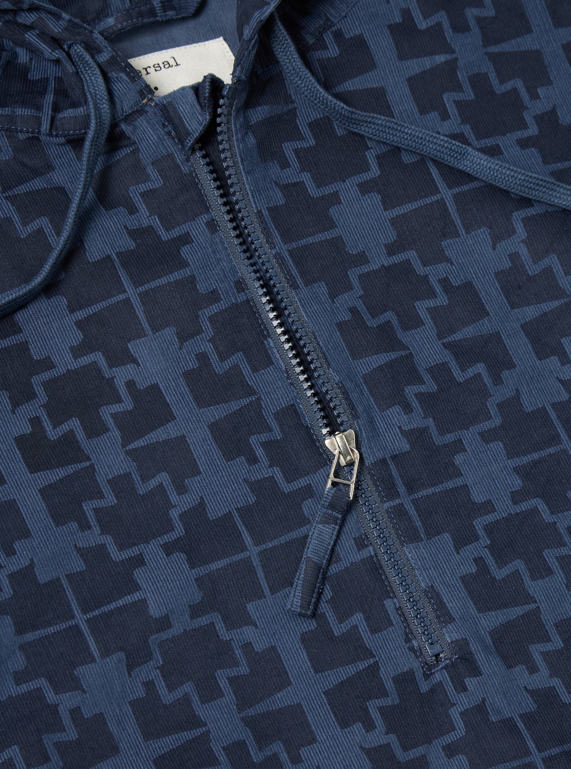 Close-up of the Navy Mitla Print Cord Liam Jacket. Features a blue corduroy material with a geometric print and a partial zipper. The background is a plain surface.