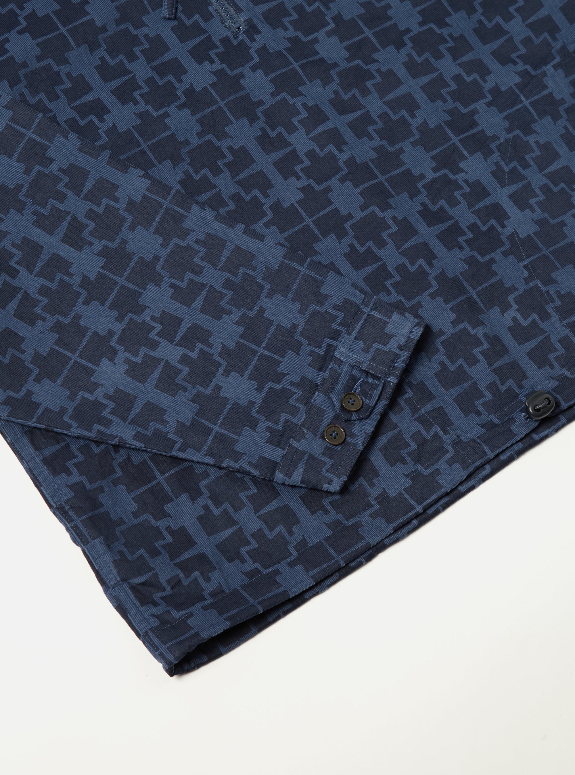 Close-up of the Navy Mitla Print Cord Liam Jacket on a white surface. The jacket features a navy geometric print and corduroy texture. Sleeve detail with button closure.