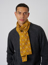 A man models the Mustard Embroidery Cotton Satin Embroidery Scarf. The mustard scarf has a geometric pattern. He wears a gray sweater against a white backdrop.