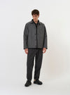 The Grey/Blue Jacquard Weave Field Jacket is shown laid flat against a solid white background. The jacket features a patterned jacquard weave in shades of grey and blue, a classic pointed collar, a five-button front closure, and two large square patch pockets near the hem. The garment has a straight-cut hem and plain cuffs.