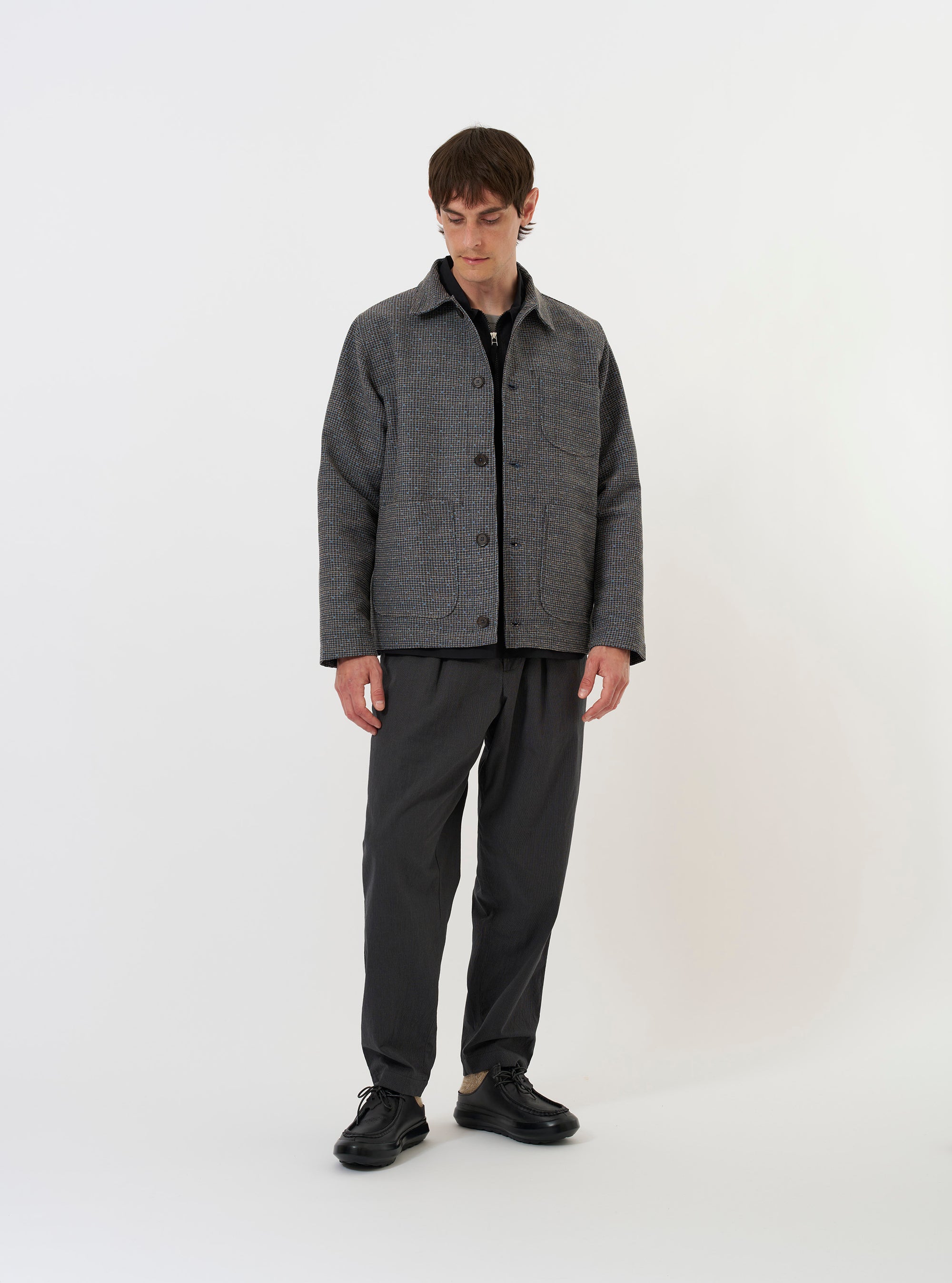 The Grey/Blue Jacquard Weave Field Jacket is shown laid flat against a solid white background. The jacket features a patterned jacquard weave in shades of grey and blue, a classic pointed collar, a five-button front closure, and two large square patch pockets near the hem. The garment has a straight-cut hem and plain cuffs.