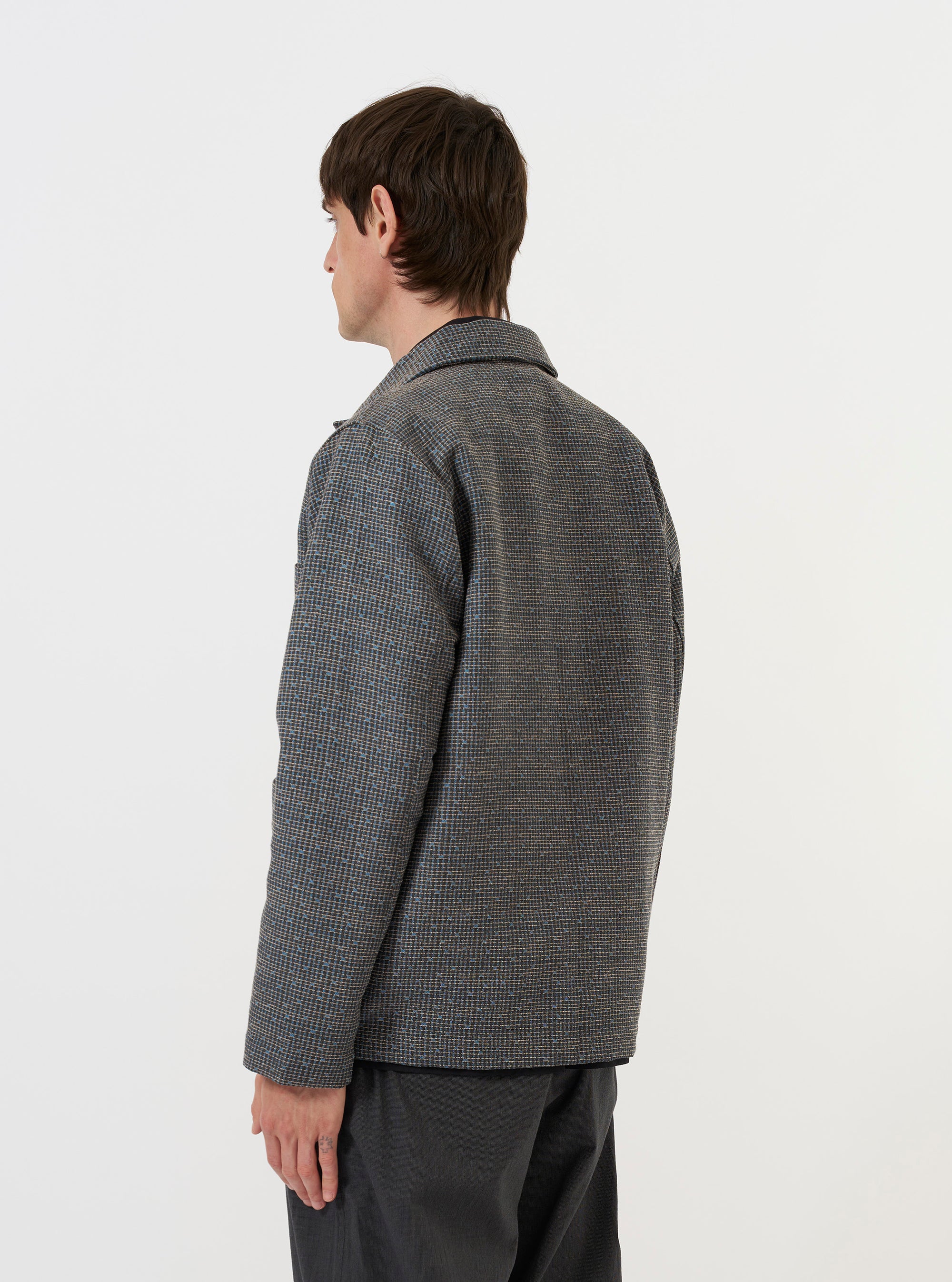 A model is wearing the Grey/Blue Jacquard Weave Field Jacket against a plain white background. The image shows the jacket from the back, highlighting the textured jacquard pattern in shades of grey and blue, a straight hem, and a classic collar.