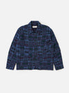 The Navy Madras Patchwork Duty Jacket is displayed flat against a solid white background. The jacket features a boxy, cropped silhouette with a vibrant blue and navy patchwork design. Prominent details include a full button-through front, a classic pointed collar, large front pockets, and long sleeves with buttoned cuffs.