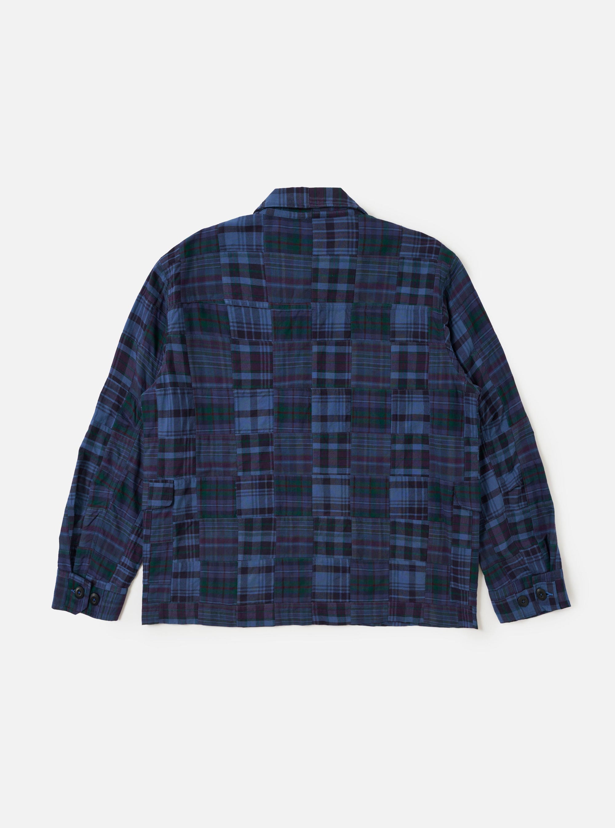 The Navy Madras Patchwork Duty Jacket is shown from the back, laid flat against a plain white background. The image highlights the patchwork construction of various blue and navy plaid cotton fabrics, the straight hem, and the loose, darted sleeves.