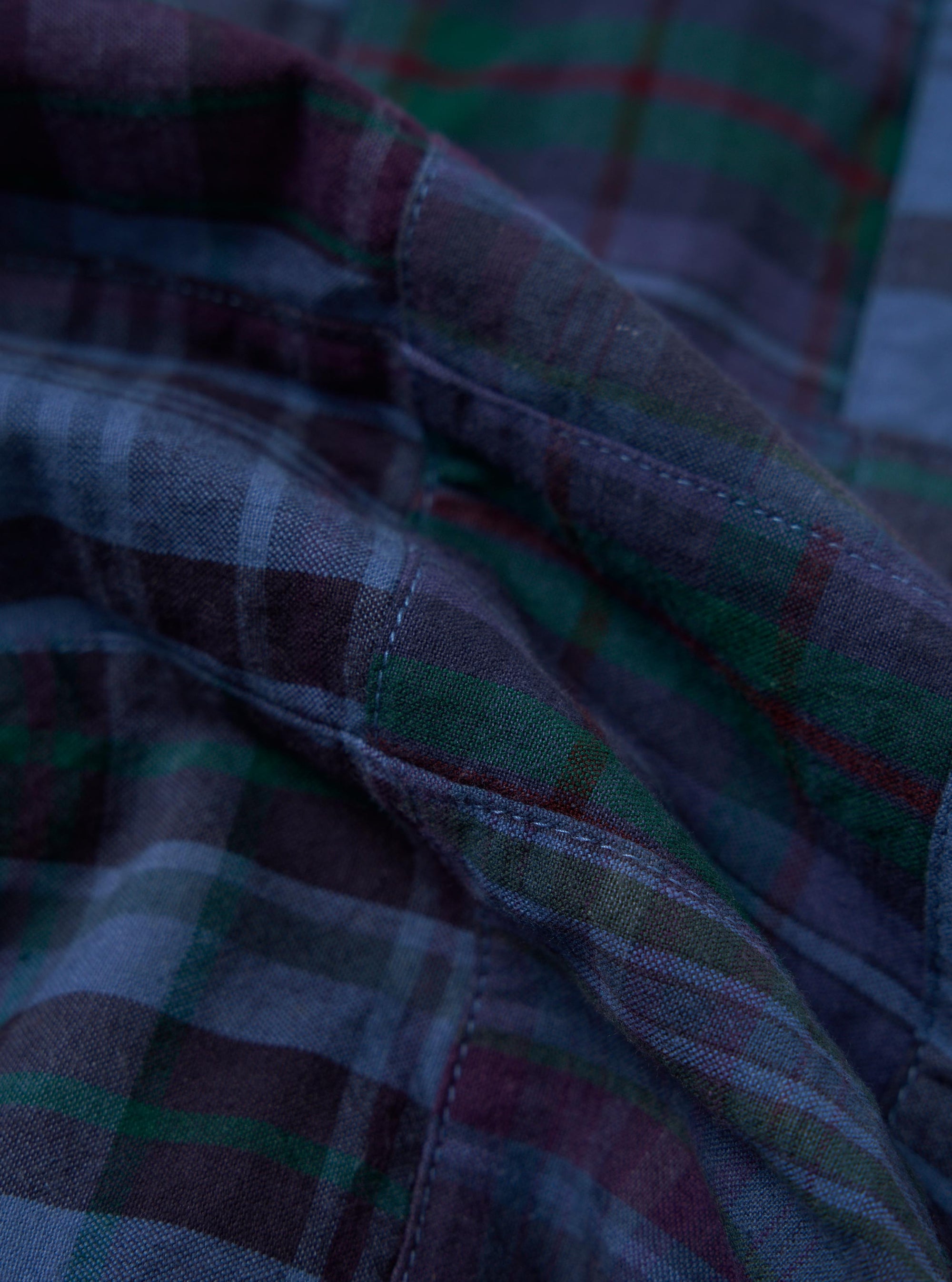 A close-up, square fabric swatch of the Navy Madras Patchwork Duty Jacket showcases an intricate patchwork design. The pattern consists of various intersecting navy, blue, and white plaid and checkered cotton fabrics, highlighting the textured weave of the material.