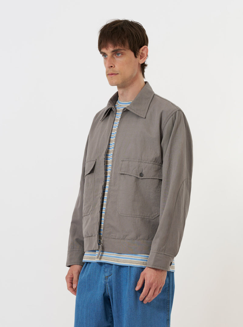 The Mid Grey Linen Slub Weave E130 Jacket is shown laid flat against a solid white background. The garment features a classic collar, a full-button front, and two large patch pockets at the hips. The mid-grey fabric has a visible textured, slubbed weave.