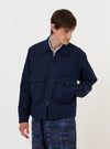 A male model is wearing the Navy Linen Slub Weave E130 Jacket against a plain white background. The jacket features a two-way zipper, a classic collar, and multiple front pockets. He is shown from the front, with the jacket zipped halfway, revealing a white top underneath.