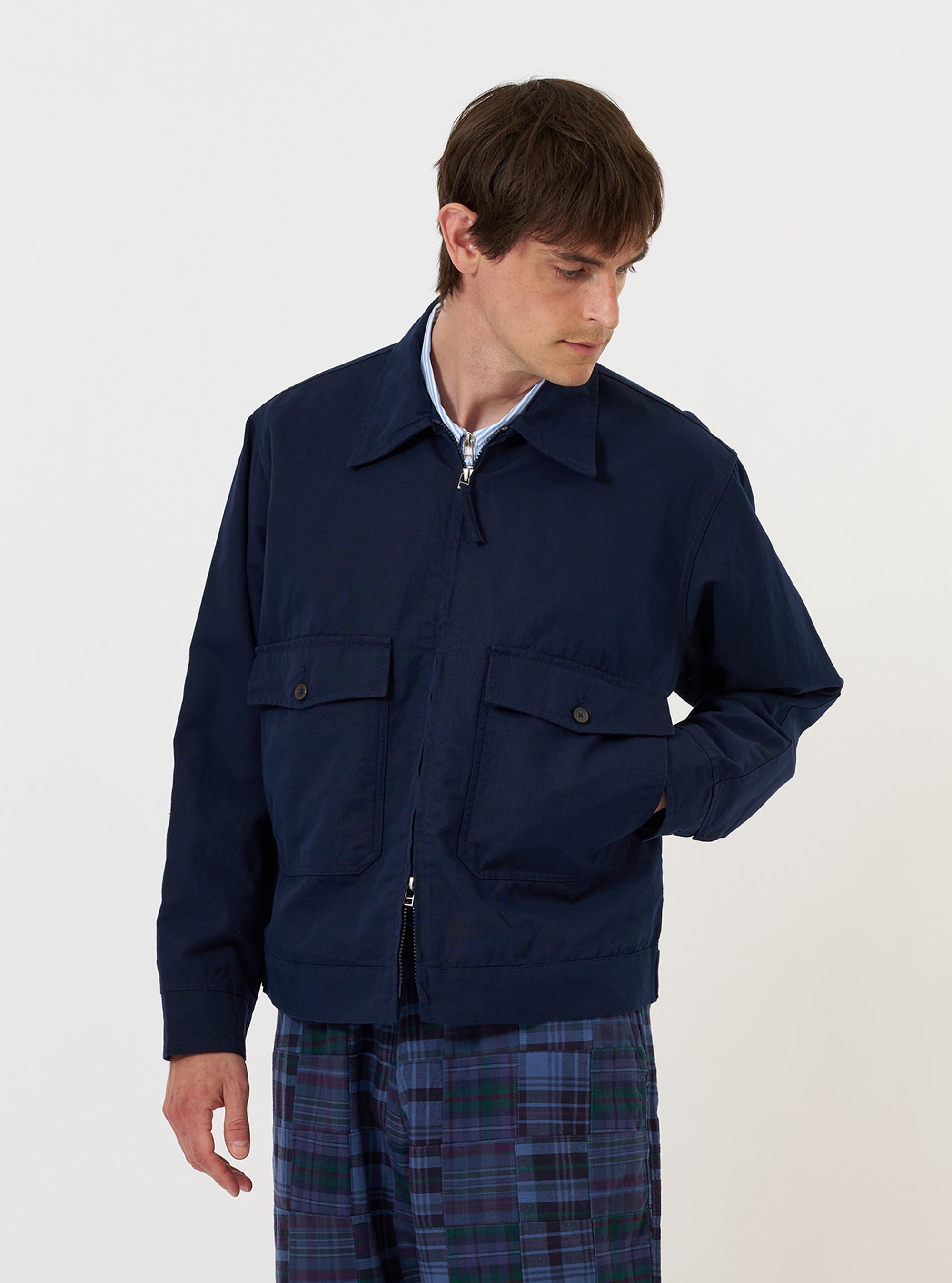 A male model is wearing the Navy Linen Slub Weave E130 Jacket against a plain white background. The jacket features a two-way zipper, a classic collar, and multiple front pockets. He is shown from the front, with the jacket zipped halfway, revealing a white top underneath.