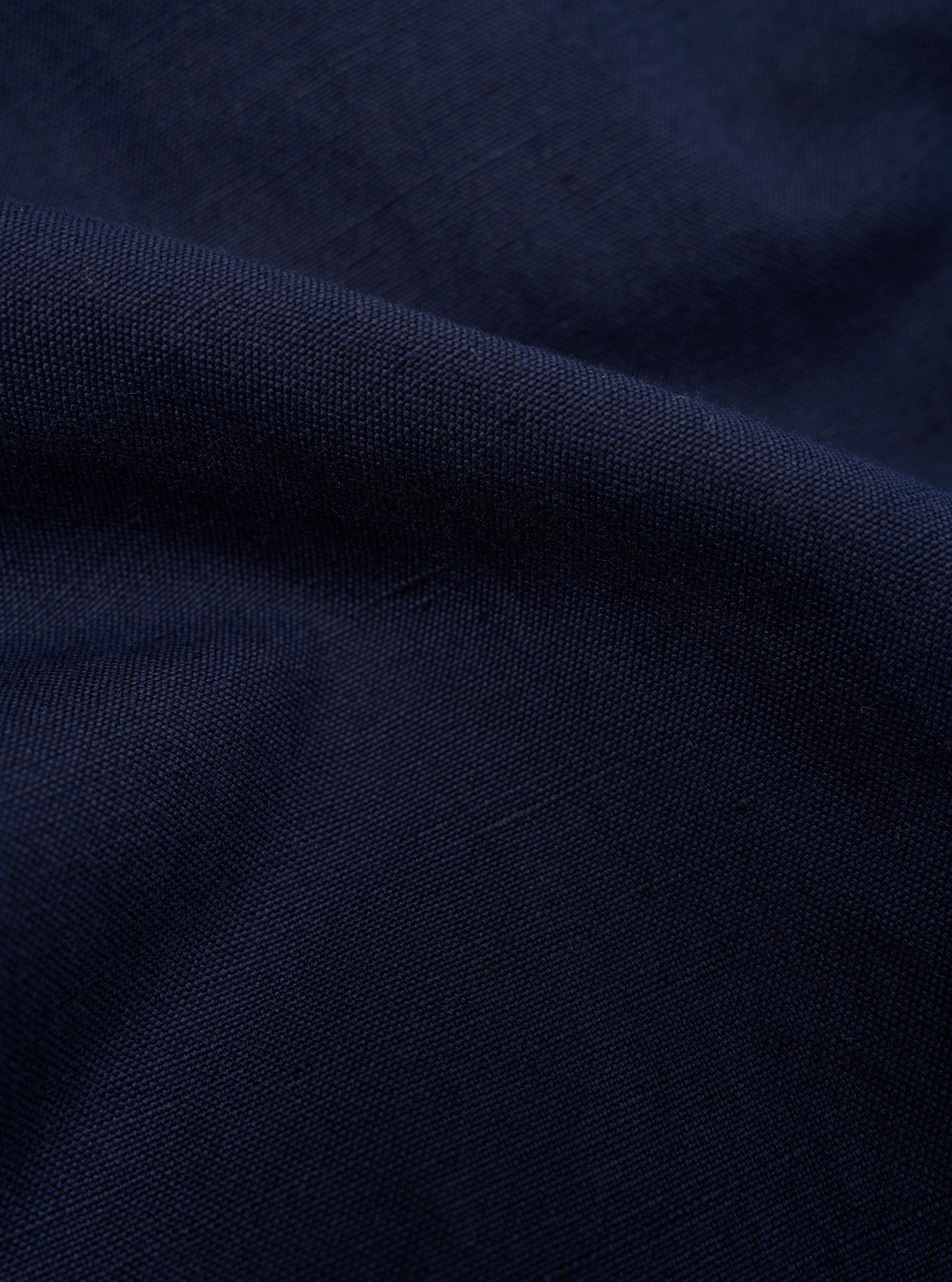 A close-up, square fabric swatch of the Navy Linen Slub Weave E130 Jacket highlights the detailed texture of the material. The fabric features a prominent slubbed yarn weave in a dark navy blue color, creating a slightly uneven and tactile surface. The swatch is shown as a flat, detailed material sample.