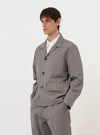 The Mid Grey Linen Slub Weave Franck Jacket is shown laid flat against a solid white background. This grey jacket features a full button front, a classic pointed collar, one chest welt pocket, and two lower flap hip pockets. The image highlights the textured, slubbed weave of the linen-cotton blend fabric.