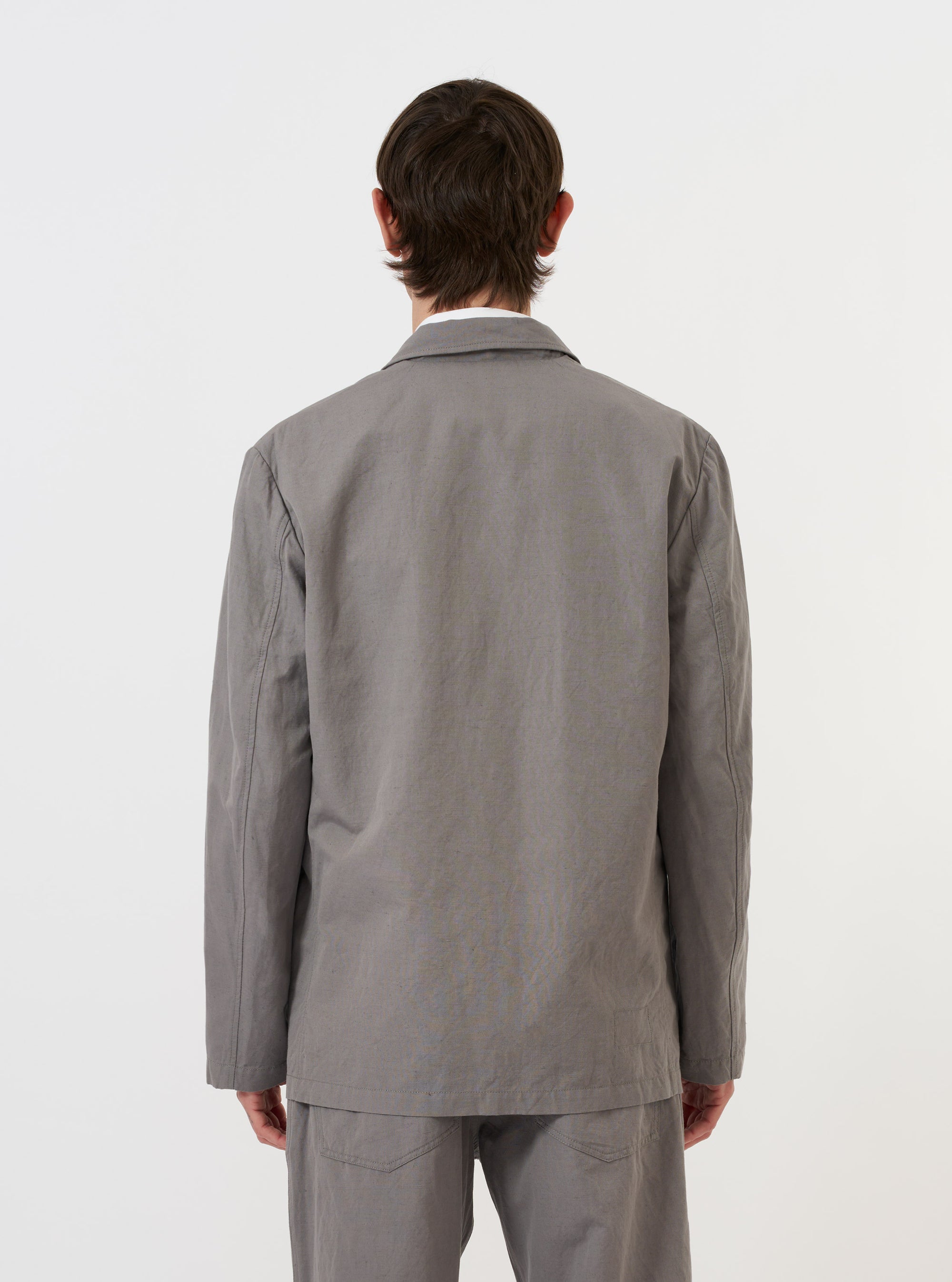 A Mid Grey Linen Slub Weave Two Button Jacket is shown from the back, laid flat against a plain white background. The image highlights the two-piece sleeve construction, a central vent at the hem, and the textured slub weave of the grey linen-cotton fabric.