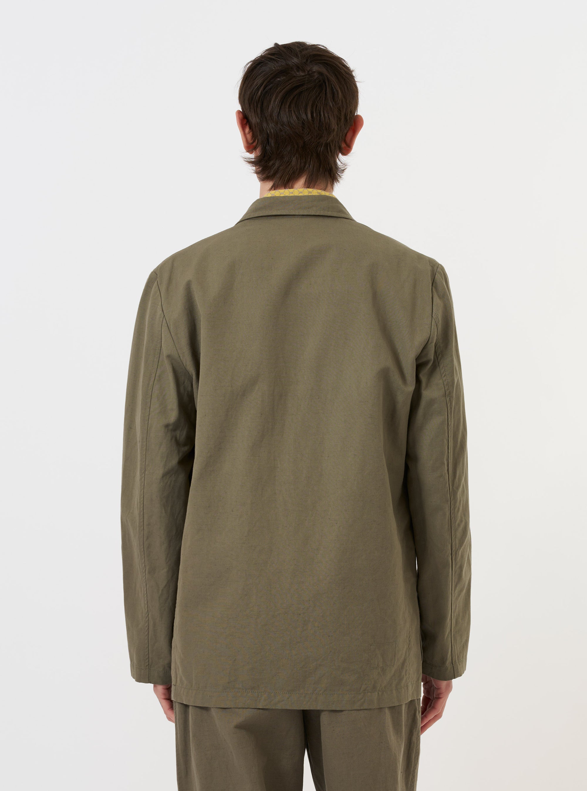 The Olive Linen Slub Weave Two Button Jacket is shown from a rear perspective, displayed flat against a plain white background. The image highlights the jacket's ventless back, structured shoulders, and the textured slub weave of the olive green fabric.