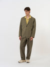 The Olive Linen Slub Weave Two Button Jacket is shown laid flat against a solid white background. The jacket features a relaxed fit, a two-button front closure, a long and wide lapel, and two large patch pockets at the hips with a smaller patch pocket on the chest. The olive green fabric has a visible textured slub weave throughout.