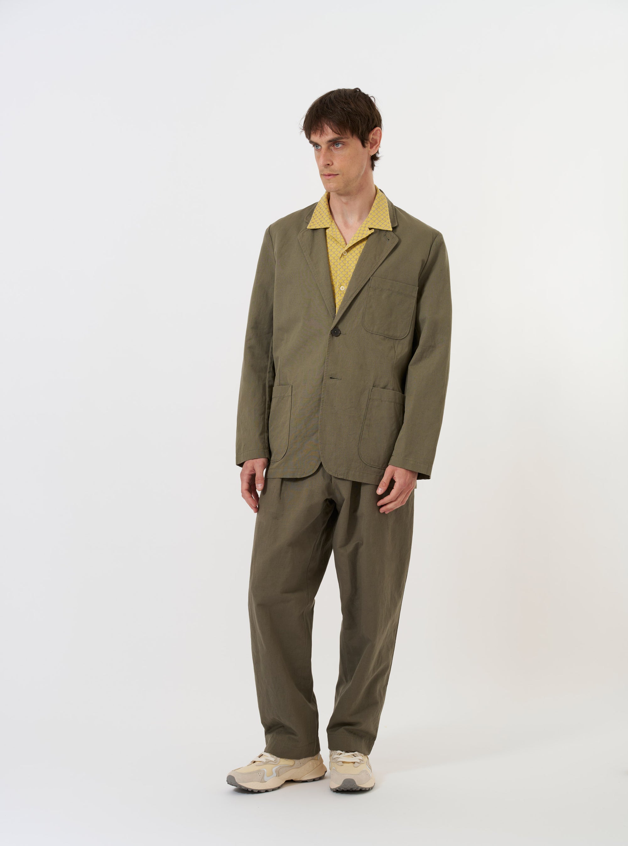 The Olive Linen Slub Weave Two Button Jacket is shown laid flat against a solid white background. The jacket features a relaxed fit, a two-button front closure, a long and wide lapel, and two large patch pockets at the hips with a smaller patch pocket on the chest. The olive green fabric has a visible textured slub weave throughout.