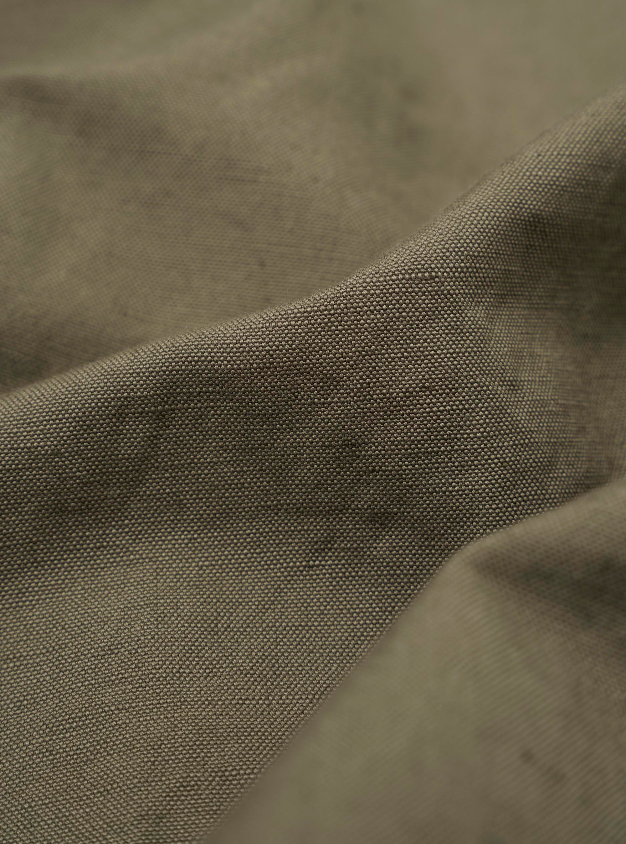 A close-up fabric swatch of the Olive Linen Slub Weave Two Button Jacket highlights the textured olive green material. The image showcases the distinct slubby appearance of the weave, characterized by visible horizontal and vertical threads.