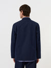 A model is wearing the Navy Linen Slub Weave Two Button Jacket against a plain white background. The image provides a side-rear view of the jacket, highlighting its relaxed fit, unstructured shoulder, and the textured slub weave of the navy linen fabric. The model is standing with their hands by their sides, and no mannequin is present.