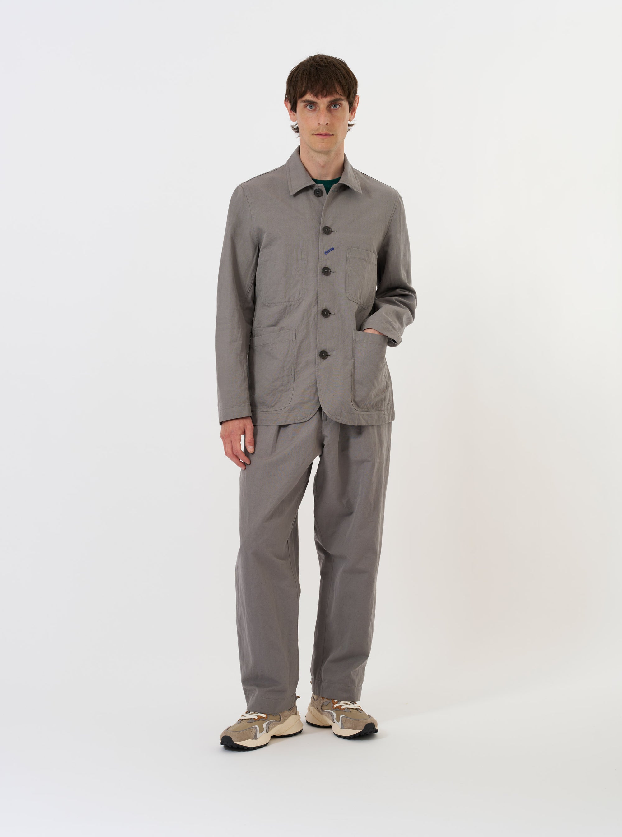The Mid Grey Linen Slub Weave Bakers Jacket is shown laid flat against a solid white background. The jacket features a classic pointed collar, a full button-down front, and four prominent patch pockets, including one on the chest and three on the lower body. The mid-grey fabric has a visible slub texture.