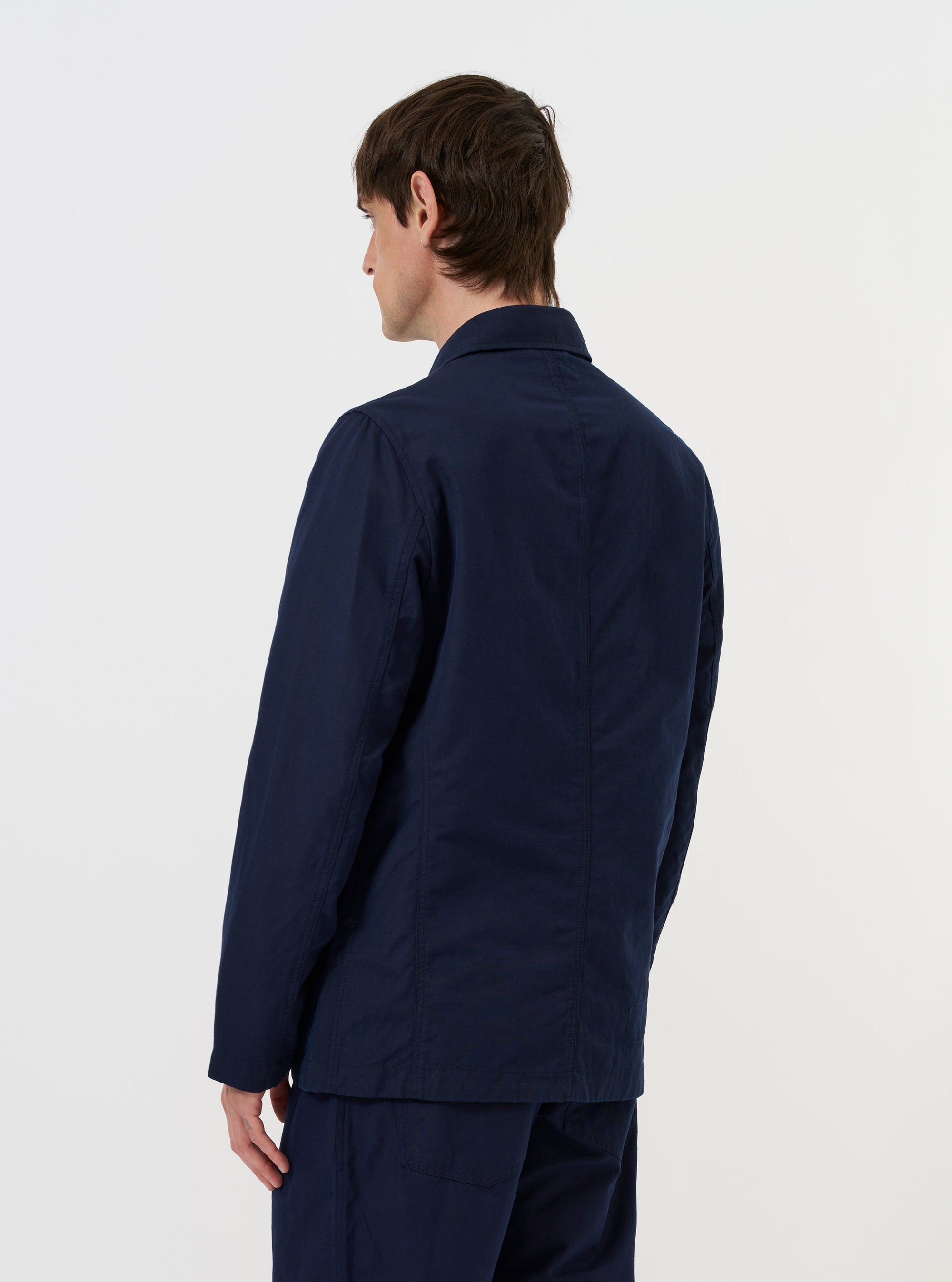 A Navy Linen Slub Weave Bakers Jacket is shown from a rear perspective, laid flat against a solid white background. The image highlights the jacket's structured back panels, straight hem, and the textured slub weave of the navy blue linen-cotton fabric.