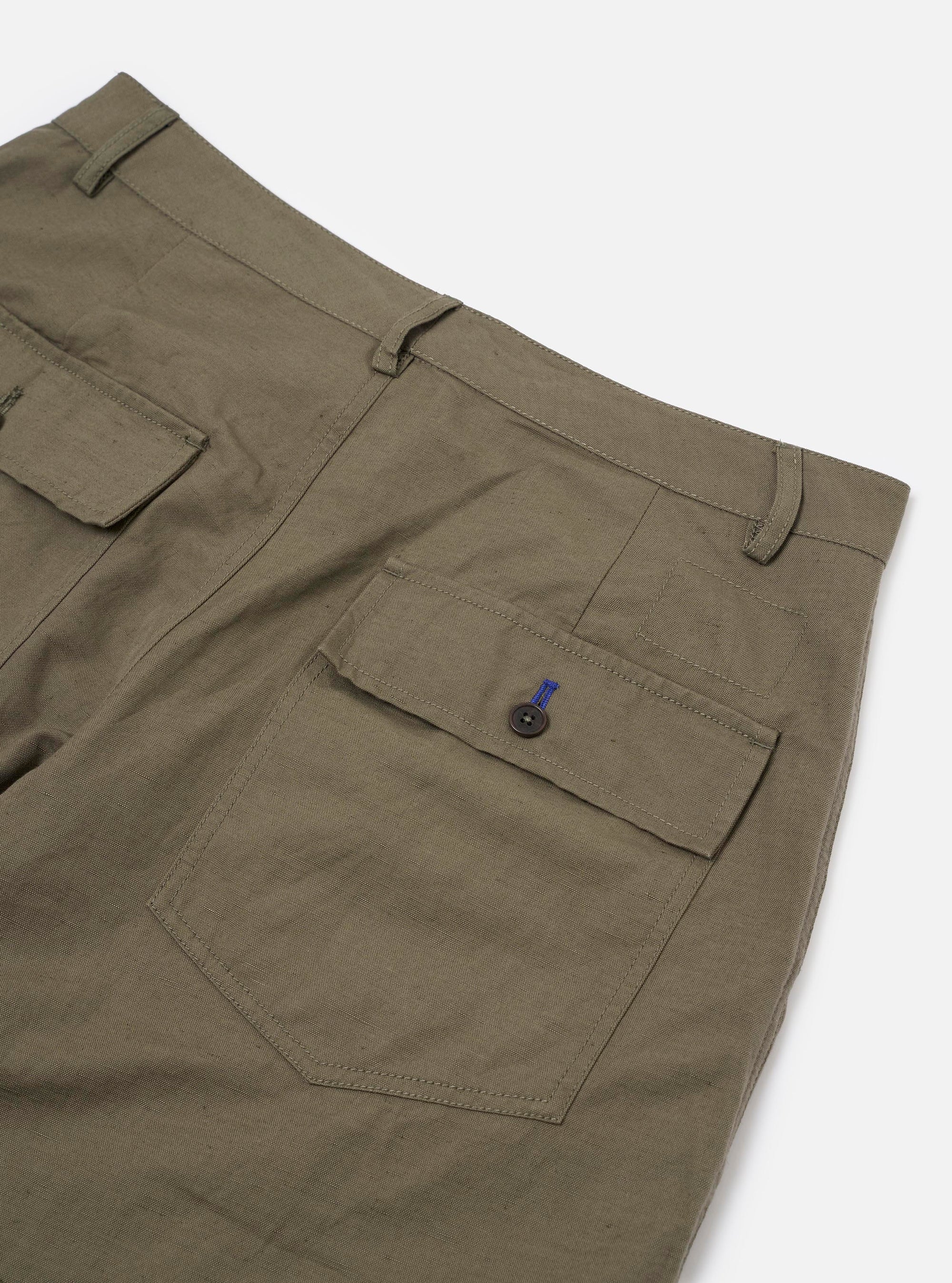 A close-up detail view of the Olive Linen Slub Weave Dizzy Trouser is displayed as a flat lay against a plain white background. The image highlights the textured slub weave of the olive green fabric, focusing on the waistband and the construction of the front pockets.