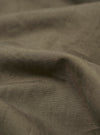 A detailed, close-up fabric swatch of the Olive Linen Slub Weave Dizzy Trouser highlights the olive green color and the textured, irregular slub weave of the material. The image focuses on the fine details of the linen-cotton blend against a neutral background.