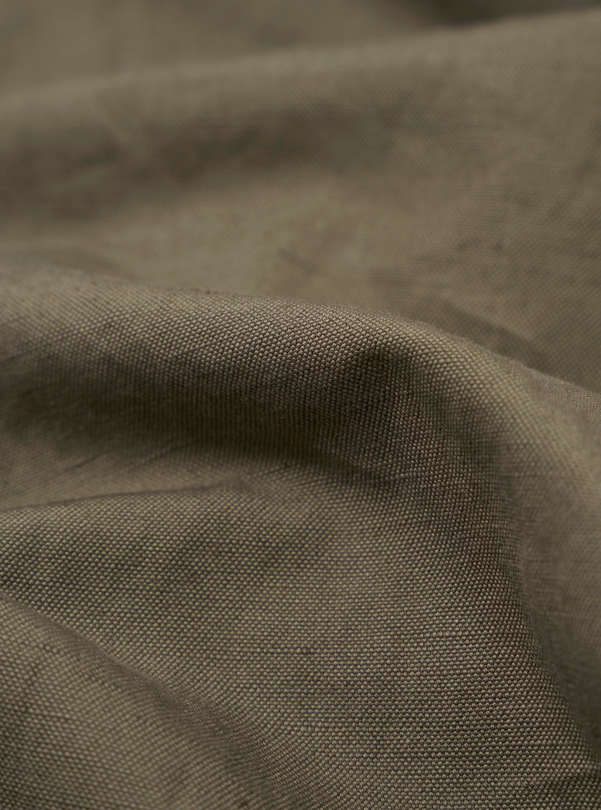 A detailed, close-up fabric swatch of the Olive Linen Slub Weave Dizzy Trouser highlights the olive green color and the textured, irregular slub weave of the material. The image focuses on the fine details of the linen-cotton blend against a neutral background.
