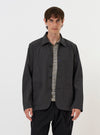 A model is wearing the Charcoal Seattle Cotton OG Bakers Jacket against a plain white background. The charcoal grey jacket is shown from the front, featuring a classic collar, a button-down front, and several large patch pockets. The model is wearing the jacket open over a light-colored top.
